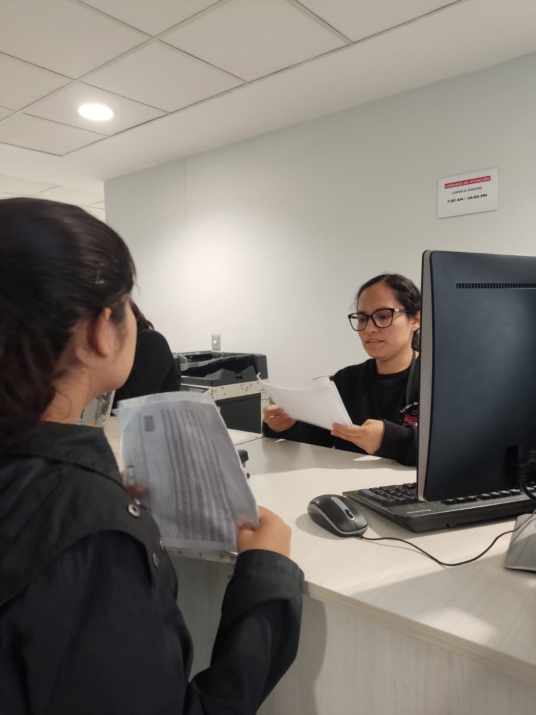 Colaboradora entregando documentos impresos a una cliente